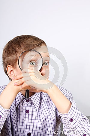 Charming blond caucasian boy in purple shirt looking through a magnifying glass in amazement Stock Photo