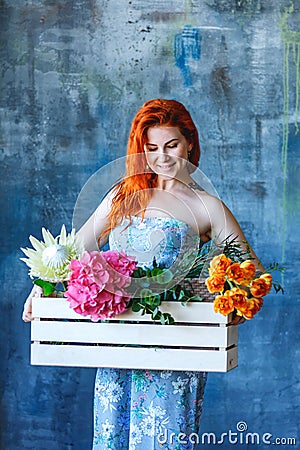Charming cheerful red hair female shop assistant holds wooden box with flowers with Hydrangea purple, freesia, protea, roses Stock Photo