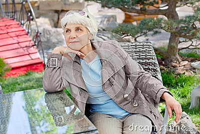 Charming elderly gray-haired woman relaxing sitting in the garden Stock Photo