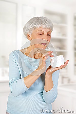 Charming elderly woman applying cosmetic cream on her face for facial skin care in bathroom at home. Stock Photo