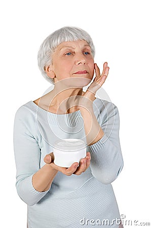 Charming elderly woman applying cosmetic cream on her face for facial skin care on a white background Stock Photo