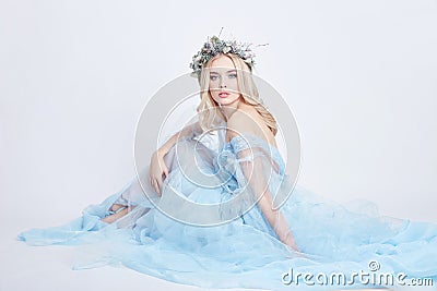 Charming fairy woman in a blue ethereal dress and a wreath on her head on white background, gentle mysterious blonde girl Stock Photo