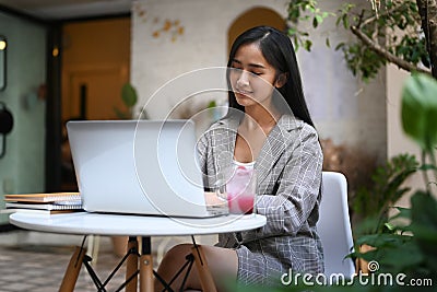 Charming female freelancer thinking about new ideas during work on laptop computer at outdoor cafe. Stock Photo