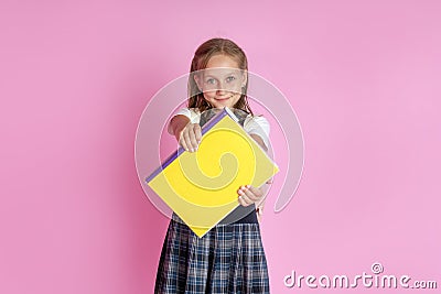 A charming girl with blond hair in a school uniform with a book in her hands on a pink background. Studio photo. Back to school Stock Photo