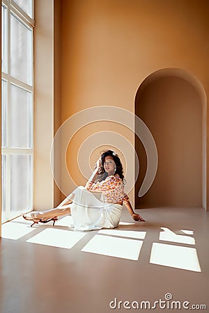 Charming lady with dark hair sitting on floor near window Stock Photo