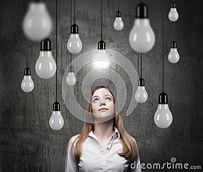 Charming lady is looking upward at the hanging light bulbs. A concept of searching new ideas. Stock Photo