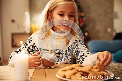 Charming little blonde girl taking delicious cookie from plate w Stock Photo