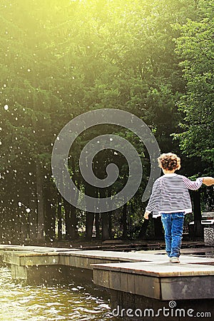 Ufa, Russia - July 31, 2013:little child walking along the edge of the fountain, holding his hand on the background of green trees Editorial Stock Photo