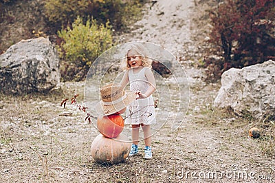 Charming little girl in a straw hat, wicker chair, pumpkins Stock Photo