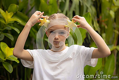 Charming little girl with two slices of fresh starfruit. Caucasian girl holding carambola in her hands. Selected focus. Green Stock Photo