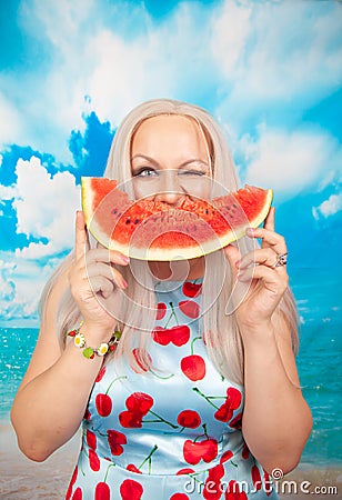 Charming plump blonde in pin up dress stands with a piece of watermelon and enjoys rest and a snack Stock Photo