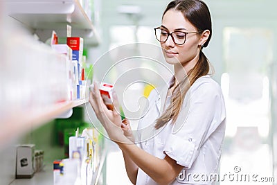 A charming smiling girl with dark hair and glasses,wearing a lab coat,takes something from the shelf in a modern Stock Photo