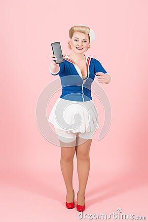 Charming stylish sailor female showing black touch screen of smart phone to the camera and pointing with finger on gadget. Stock Photo
