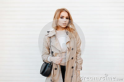 Charming stylish young woman in trendy spring coat in white t-shirt with black fashionable leather bag Stock Photo