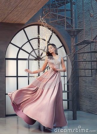 Charming tender princess in long peach pink shiny satin flying waving dress with neckline, girl stands on vintage stairs Stock Photo