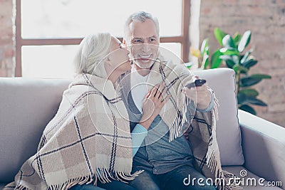 Charming two elderly people are sitting on a couch at home resting relaxing at the weekend talking and watching tv. The man is ch Stock Photo