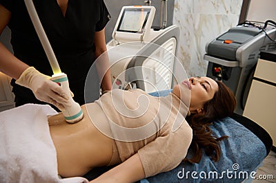 Charming woman receives anti-cellulite and anti-fat therapy in spa salon. Ultrasonic cavitation body contouring treatment Stock Photo