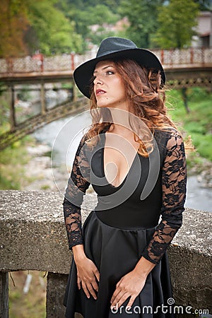 Charming young light brown hair brunette woman with big black hat and blouse with lace sleeves. gorgeous young woman with cur Stock Photo