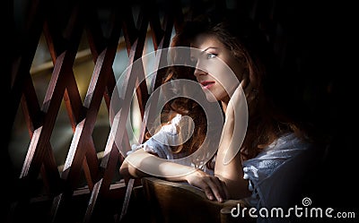 Charming young light brown hair woman looking through wooden grid. gorgeous young woman with long curly hair staying in rays Stock Photo