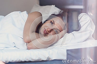 Beautiful young woman wakes up in her bed fully rested. A woman with a gentle smile in bed after waking up. Stock Photo