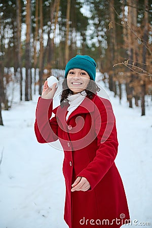 Charming young woman plays, throws a snowball, smiles at the camera with a cheerful toothy smile. Outdoor leisure activity on a Stock Photo