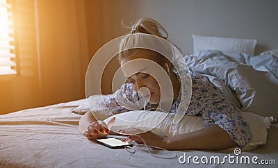Charming young woman with ponytail listening to good music while lying on comfortable bed Stock Photo