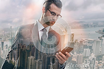 Chat with client. Handsome bearded businessman in suit using smart phone while standing against of morning cityscape Stock Photo