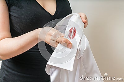 Cheating and infidelity concept. Woman holds white shirt of her husband with red lipstick stains. Stock Photo