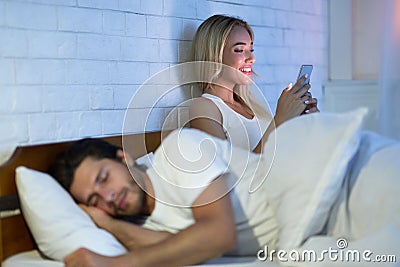 Cheating Wife Chatting On Cellphone While Husband Sleeping In Bedroom Stock Photo