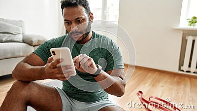 Check results. Young man using smartphone app while having morning workout at home. Freshman relaxing after training Stock Photo