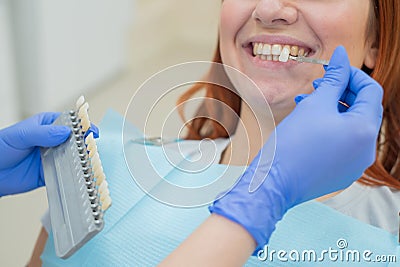 Check and select the color of the teeth in the dentist chair. Dentist makes the process of treating a beautiful young red-haired Stock Photo