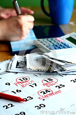 A checkbook, bills, a calculator, a calendar and a person writing on a checkbook Stock Photo