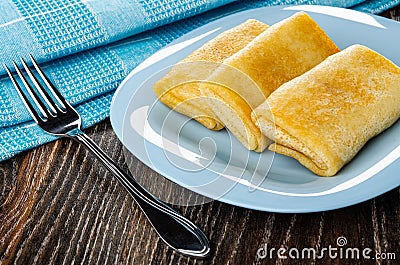 Napkin, fork, fried pancake rolls in blue plate on wooden table Stock Photo