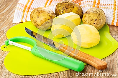 Napkin, unpeeled potatoes, peeler, knife, peeled potato on cutting board on wooden table Stock Photo