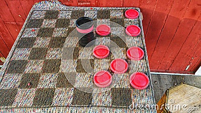 Checkers anyone?! Outdoor cloth board with large red and black checkers. Red wood wall. Competition. Stock Photo