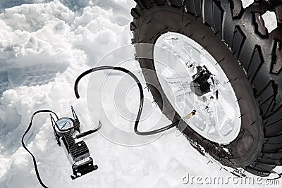 Checking tire pressure. Pumping air into auto wheel on the ATV 4wd quad bike stand in heavy snow. Stock Photo
