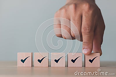 Checklist Survey and assessment concept, human hand putting cube wood with Check mark icon on wooden blocks, gray background Stock Photo
