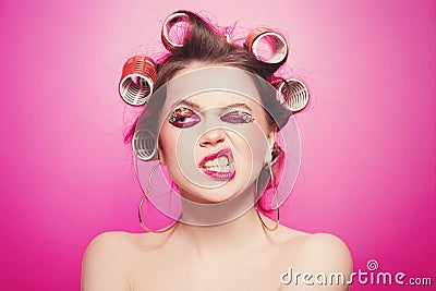 Cheeky girl posing on pink background in body, with curlers on head. Pretty woman with sweet makeup in studio Stock Photo