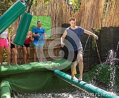 Cheerful guy balancing on soft log between swinging bags over pool with water Stock Photo