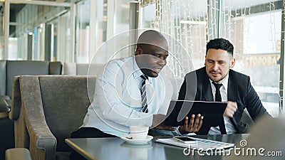 Cheerful African American businessman in formal clothes using digital tablet discussing startup project with his stock footage Cheerful African American businessman in formal clothes using digital tablet discussing startup project with his stock footage