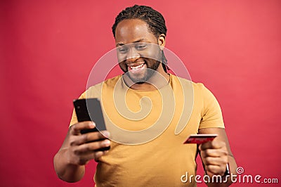 Cheerful African-American guy shopping online isolated on red Stock Photo