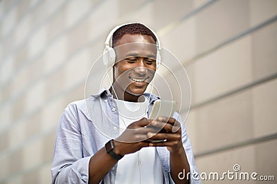 Happy African American man in headphones picking music playlist on smartphone near brick wall outside Stock Photo