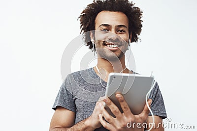 Cheerful african man in headphones smiling holding tablet looking at camera. White background. Stock Photo