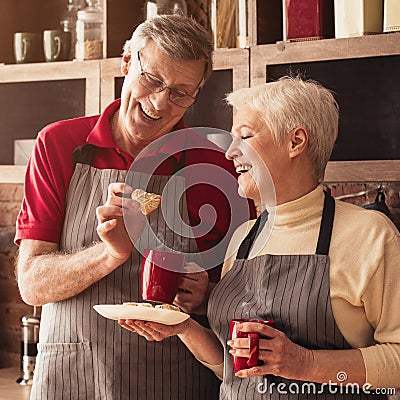 Cheerful Aged Couple Eating Homemade Cookies And Drinking Tea In Kitchen Stock Photo