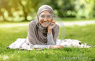 Cheerful arab girl in hijab lying on grass at park Stock Photo