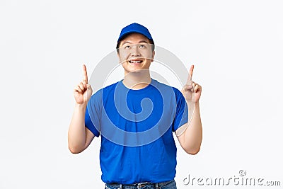 Cheerful asian delivery guy with braces, wearing blue uniform, pointing and looking at top advertisement, demontrate Stock Photo
