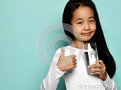 Cheerful asian girl in white longsleeve standing with glass of pure water and showing thumbs up sign Stock Photo