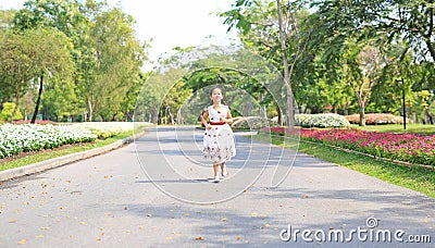 Cheerful asian little girl in white dress running on road in garden Stock Photo