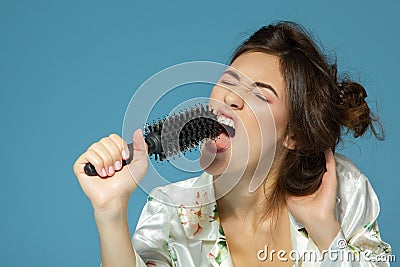 Cheerful attractive teen girl sing song holding comb like a microphone in the morning, over blue Stock Photo