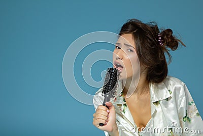 Cheerful attractive teen girl sing song holding comb like a microphone in the morning, over blue Stock Photo